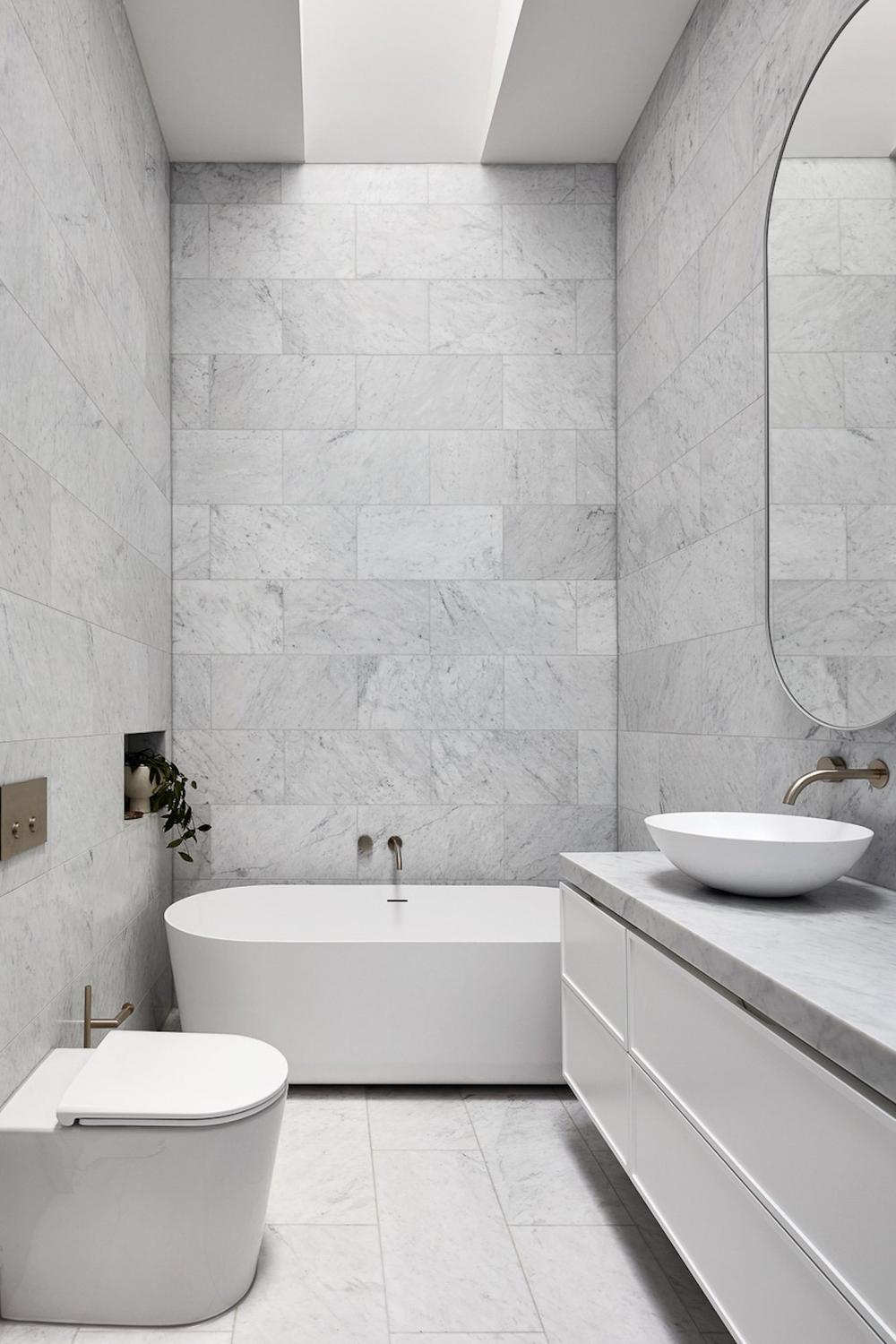 Light gray marble tiles in a modern small bathroom with a freestanding tub and gold fixtures