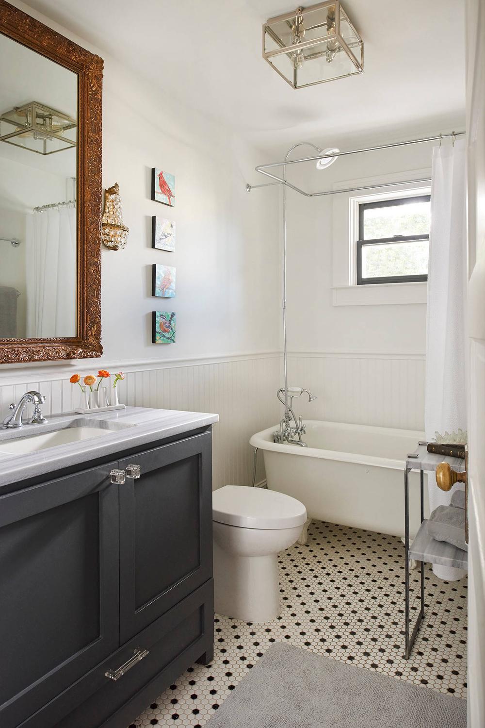 Classic small bathroom featuring a vintage-style freestanding bathtub, dark vanity, and decorative wall art.