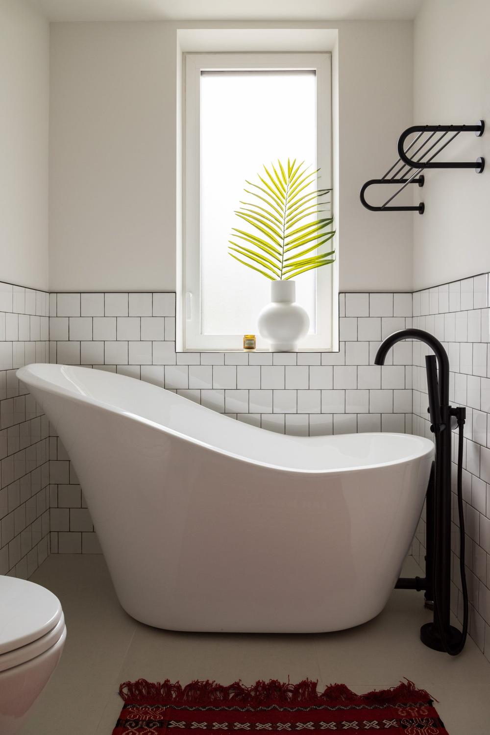 Modern bathroom featuring a stylish freestanding bathtub, large window, and decorative plants for a chic atmosphere.