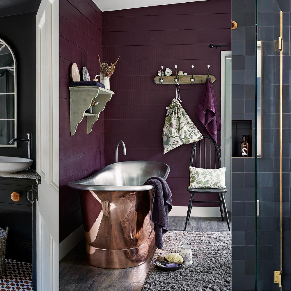 Stylish small bathroom with freestanding copper bathtub and rich plum walls.