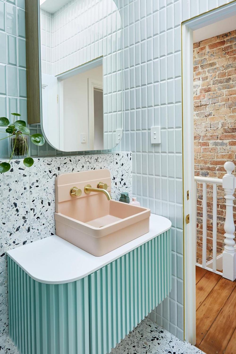 A stylish bathroom with mint green tiles, a pink basin, and modern fixtures, creating an elegant design.