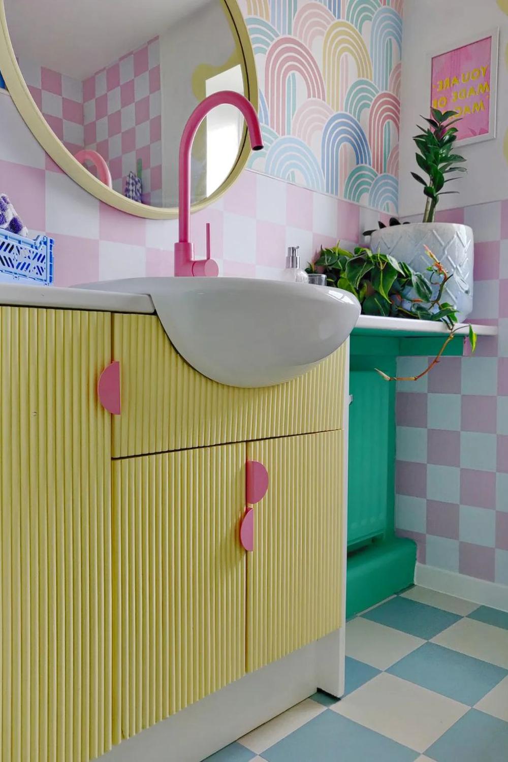 A cheerful bathroom featuring pastel pink and light blue checkered tiles, a unique pink faucet, and natural green accents.