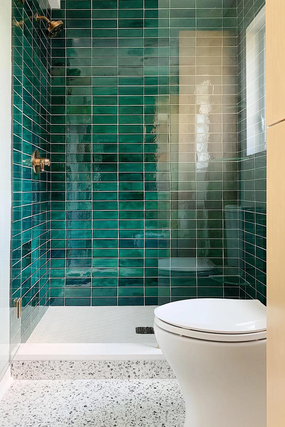 A beautiful bathroom featuring dark green subway tiles and luxury gold fixtures.