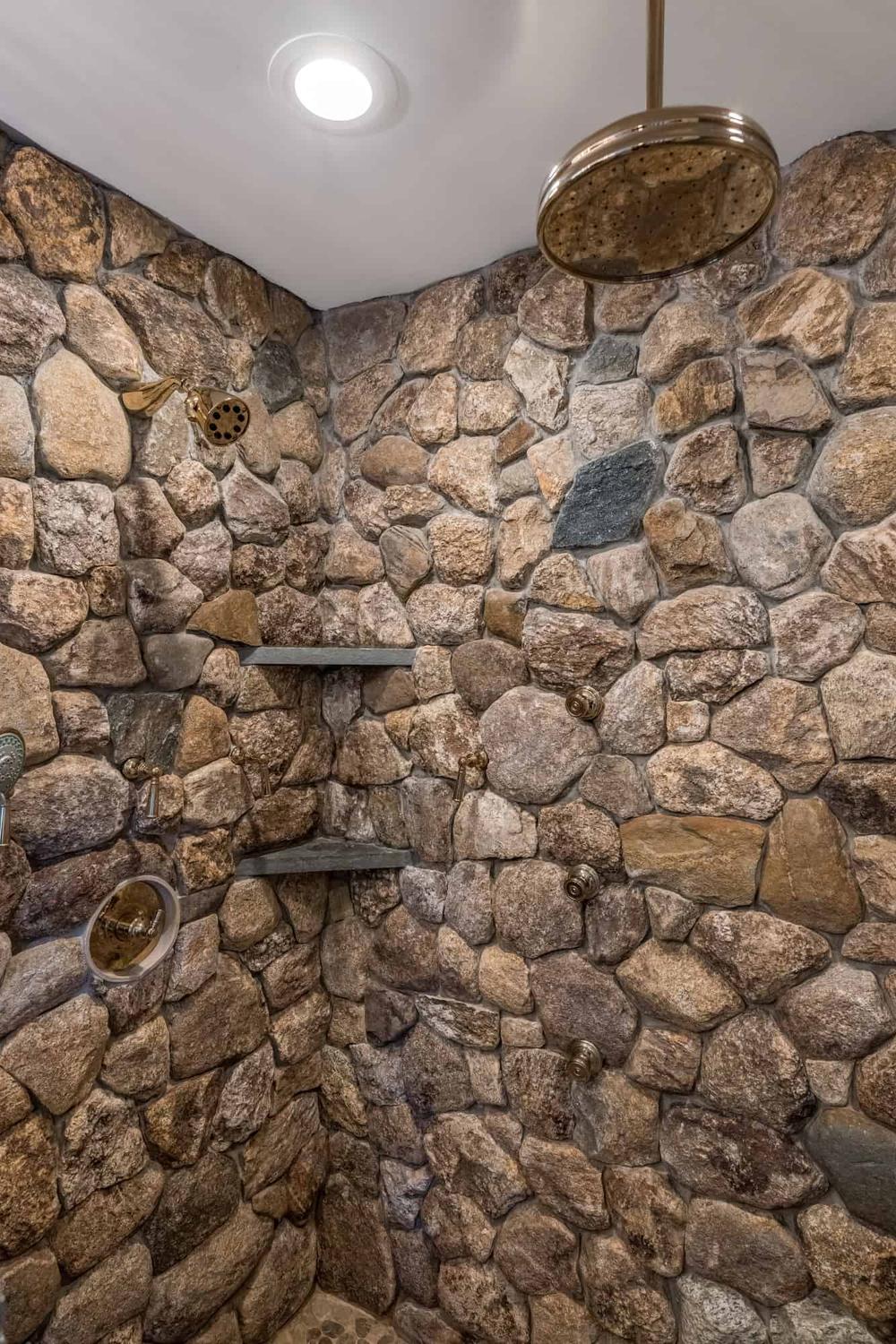 Rustic stone shower with mosaic natural stone walls, rain showerhead, and vintage-style shower knobs.