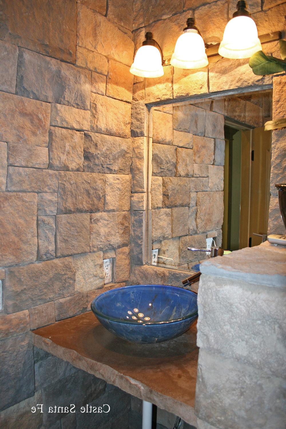 Rustic bathroom featuring rough stone walls, blue glass sink, and warm pendant lighting.