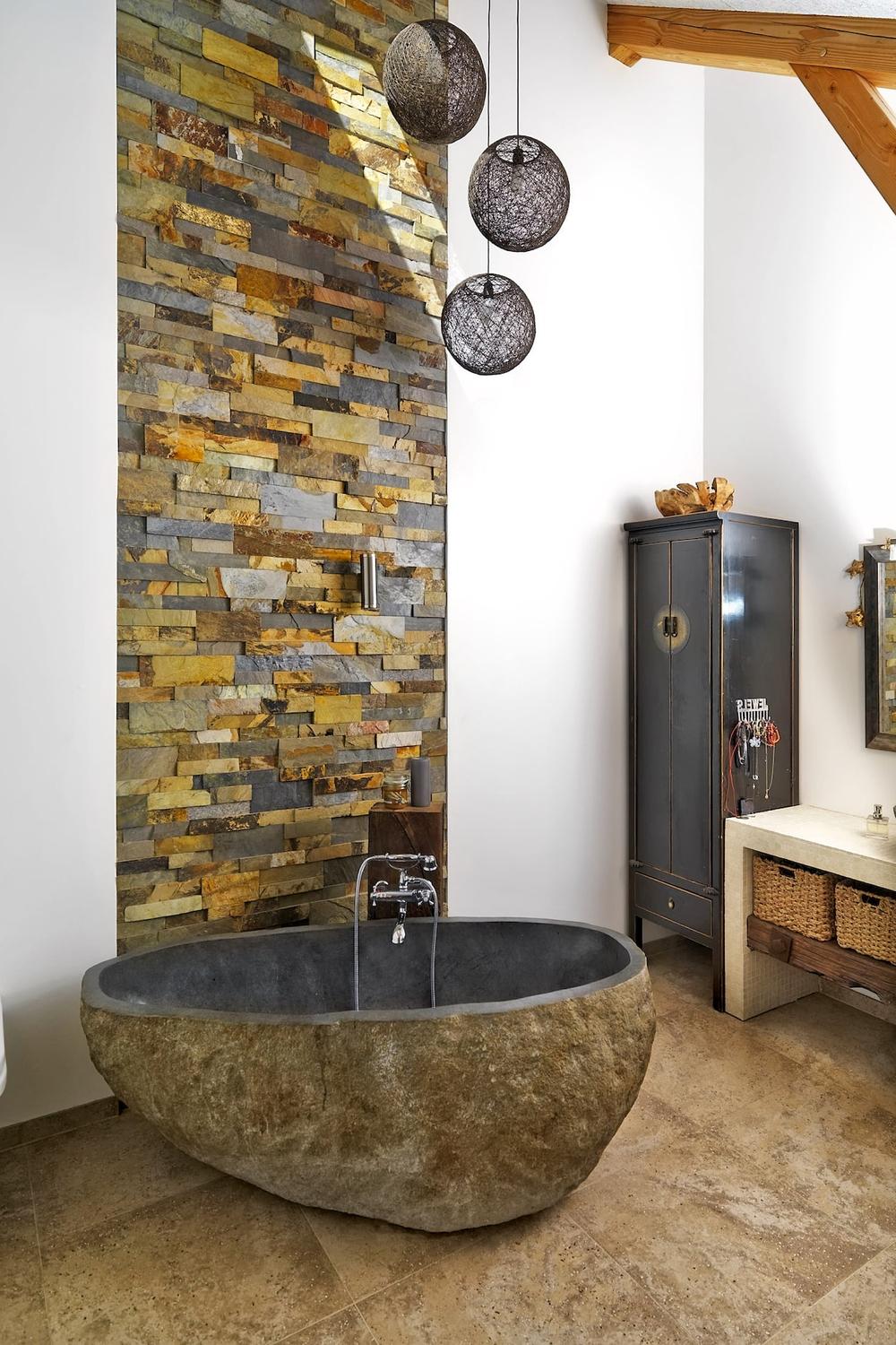 Stylish bathroom with oval stone tub, textured feature wall, and pendant lighting.