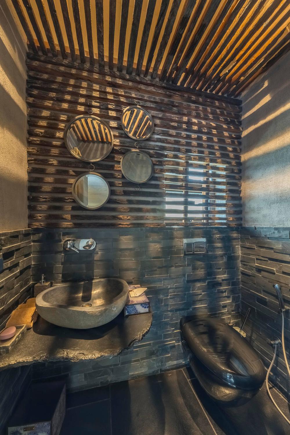 Modern bathroom with horizontal wooden slat wall, circular mirrors, and sleek stone sink.