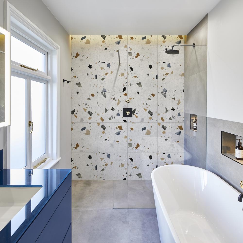 Modern bathroom with striking terrazzo wall, freestanding bathtub, and stylish storage.