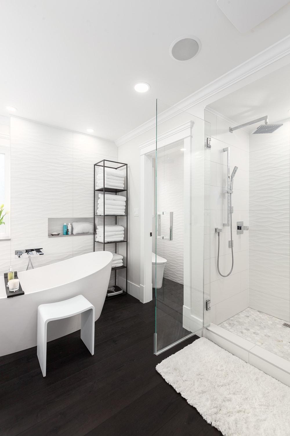 Minimalist bathroom with sleek oval freestanding bathtub, dark wood floor, and modern shower design.