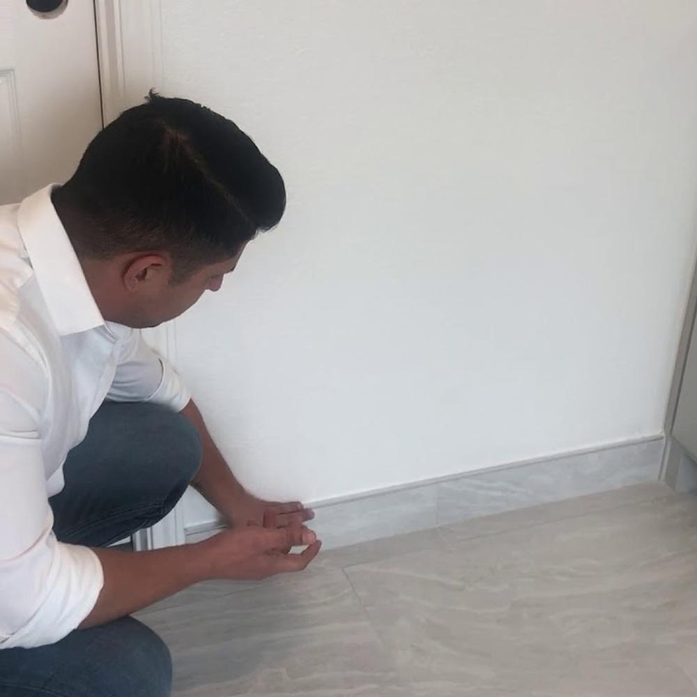 Man inspecting a bathroom's clean baseboard near tile flooring.