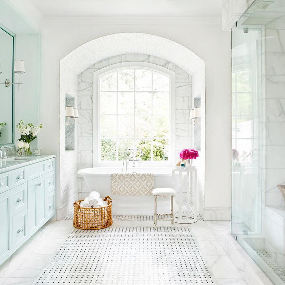 Timeless bathroom design with pastel colors, marble surfaces, and a freestanding tub under an elegant arched window.
