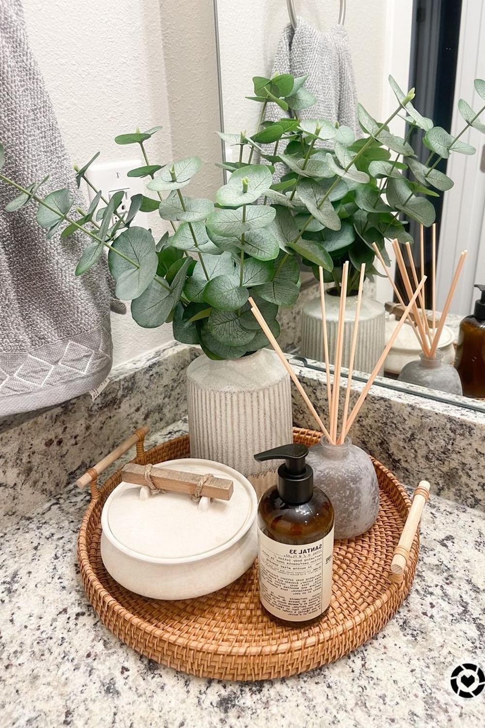 Woven round natural vanity tray with a eucalyptus display and a diffuser beside it.