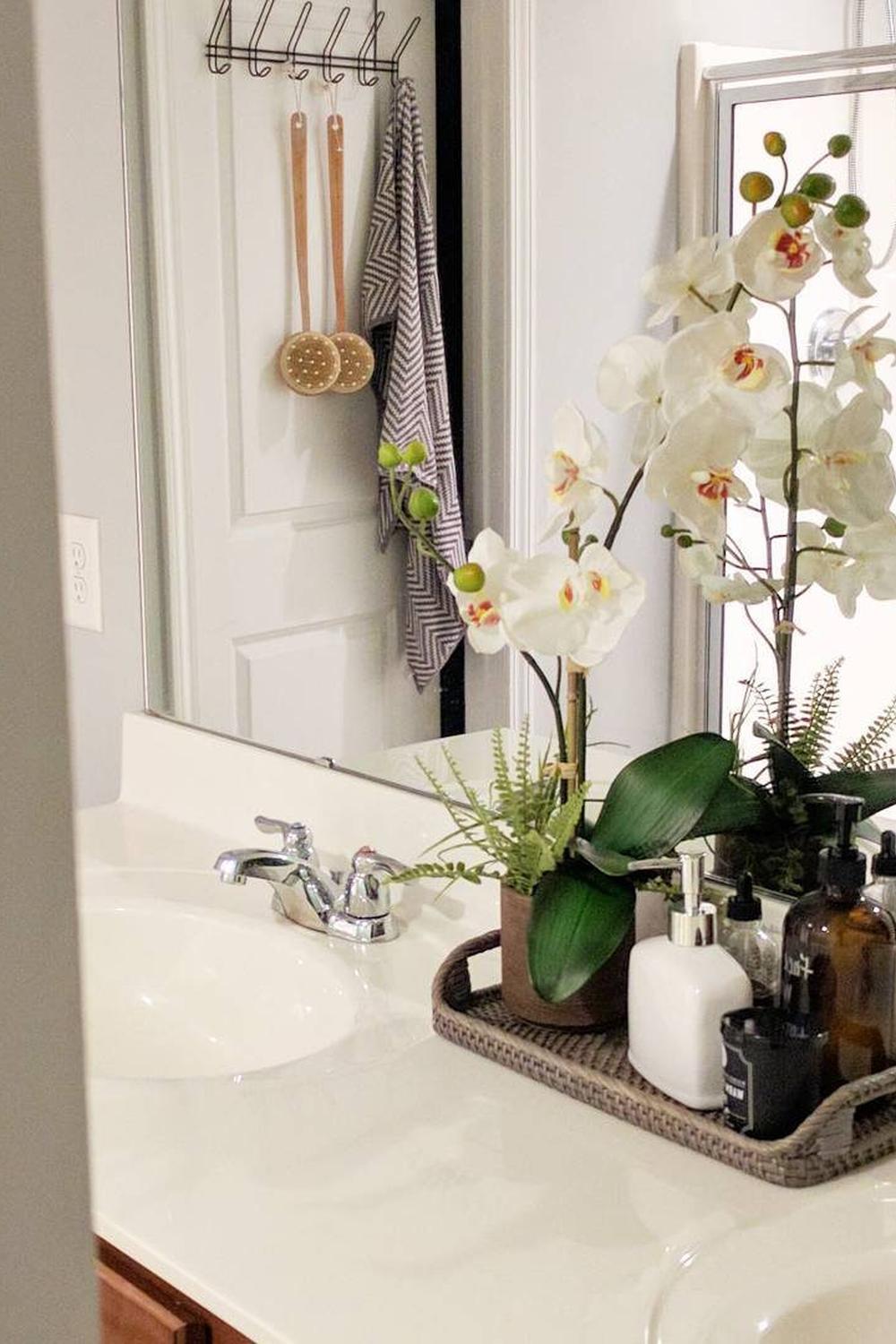 Rectangular rattan vanity tray featuring an orchid plant and various bathroom essentials.