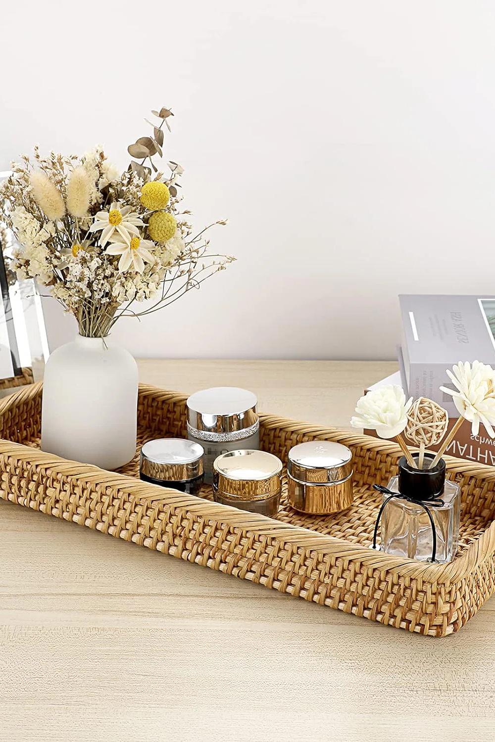 Earthy rectangular woven vanity tray with dried flowers and cosmetic containers.