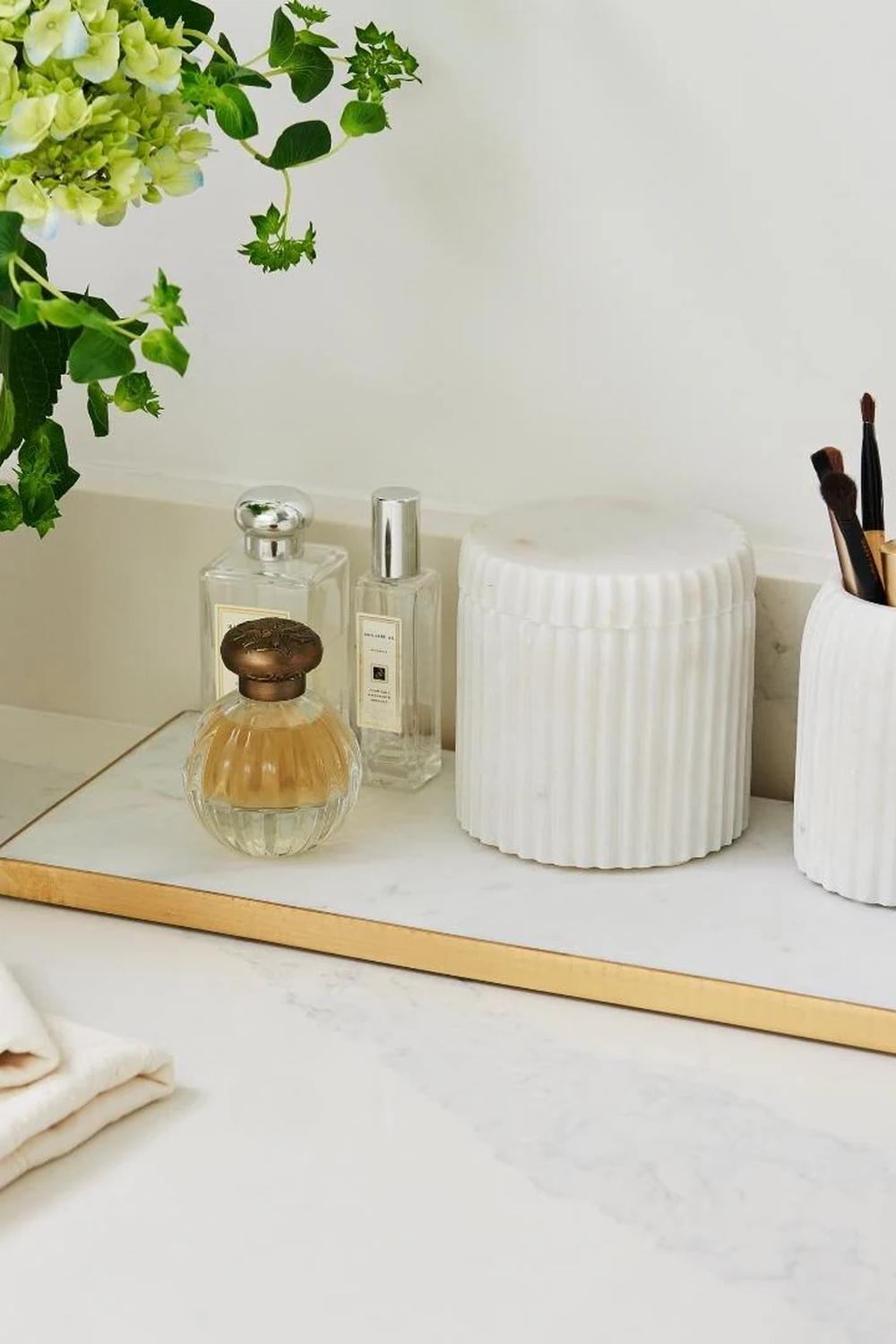 Rectangular marble vanity tray with a gold border holding perfume bottles and a makeup brush holder.