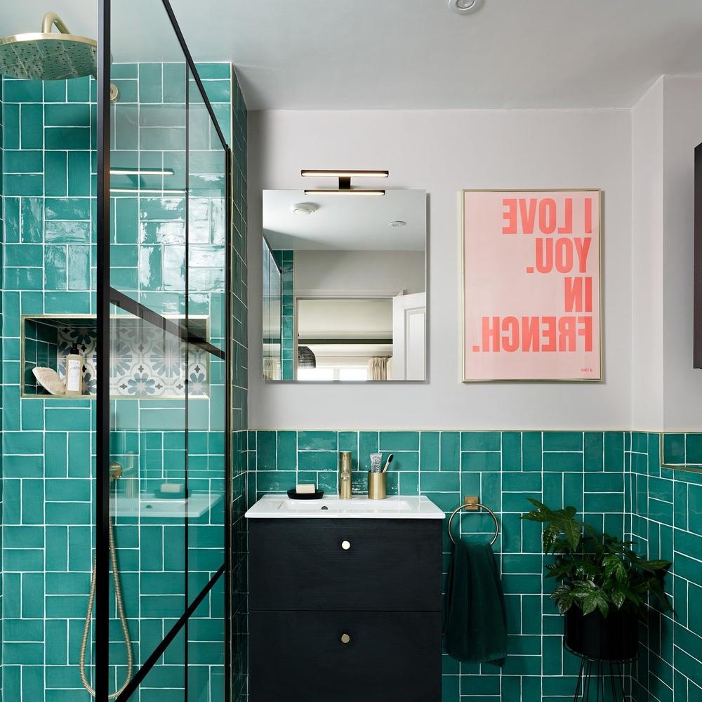 A bathroom with glossy teal tiles, minimalist black vanity, and elegant decor