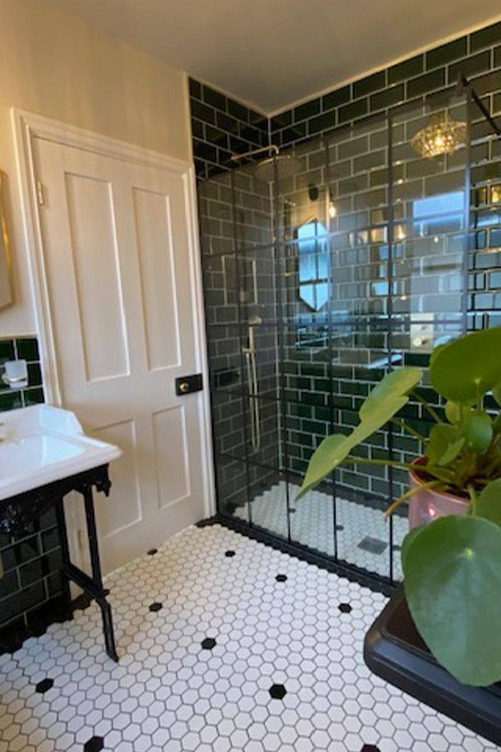 A Victorian bathroom showcasing dark green tiles and a stylish glass enclosure for the shower.