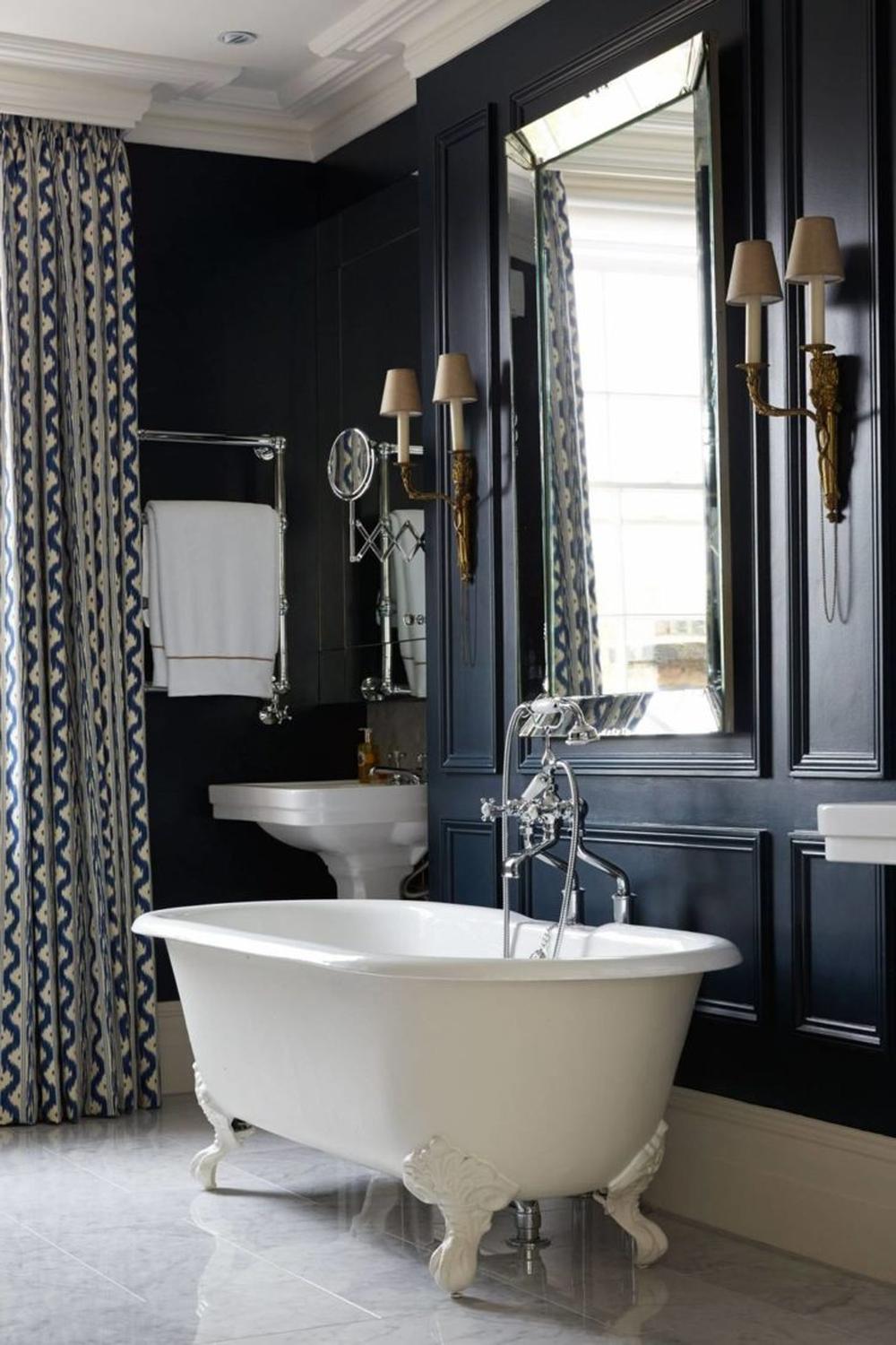 A sophisticated Victorian bathroom with dark navy walls and a luxurious clawfoot tub.