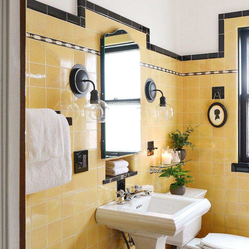 Vintage bathroom with bright yellow tiles, black accents, and an arched mirror reflecting the cheerful space.