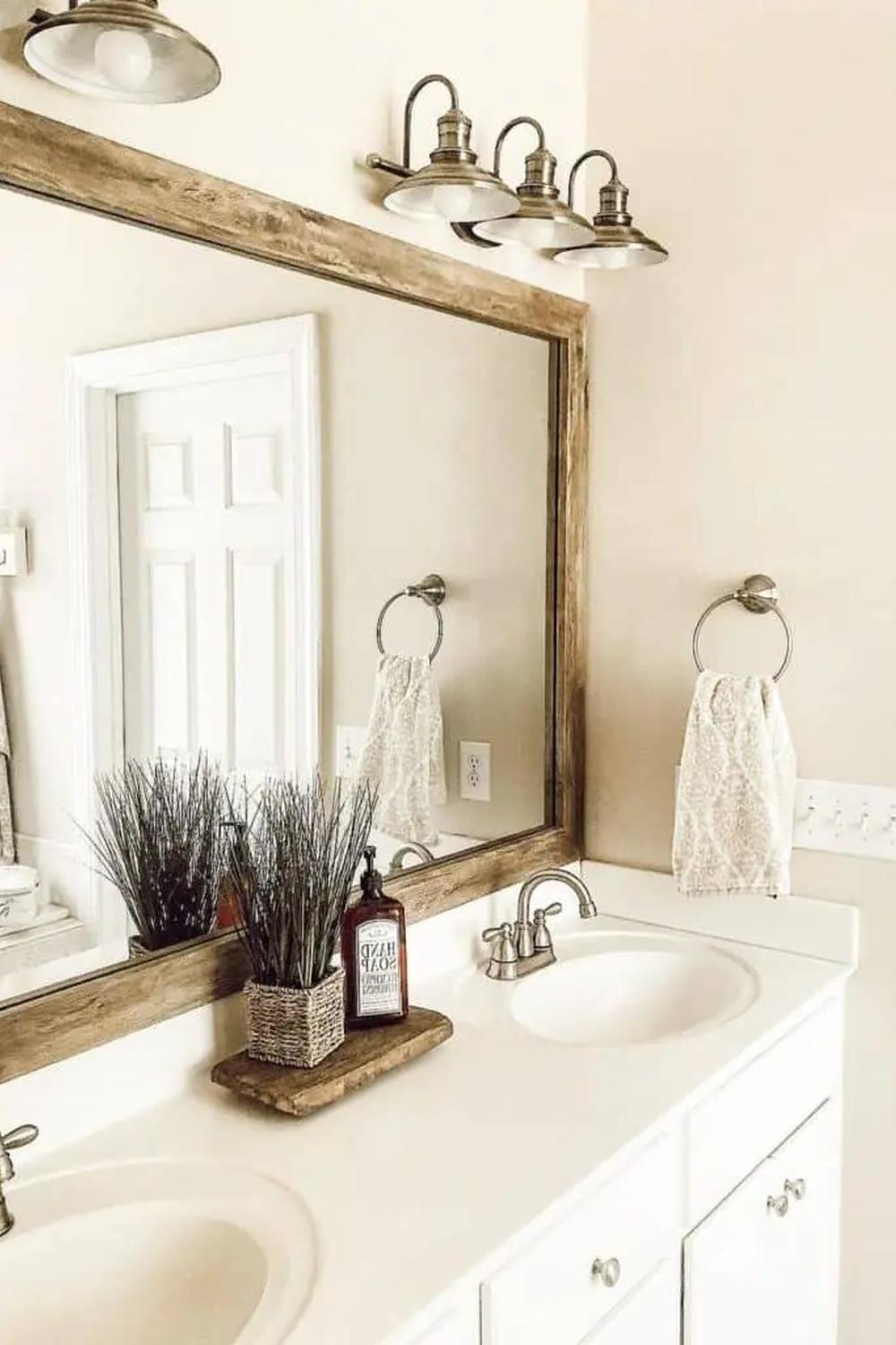 Beautifully designed white bathroom featuring wood accents, showcasing a blend of modern and rustic elements. A large mirror framed with distressed wood, dual sinks, and warm lighting create an inviting atmosphere.