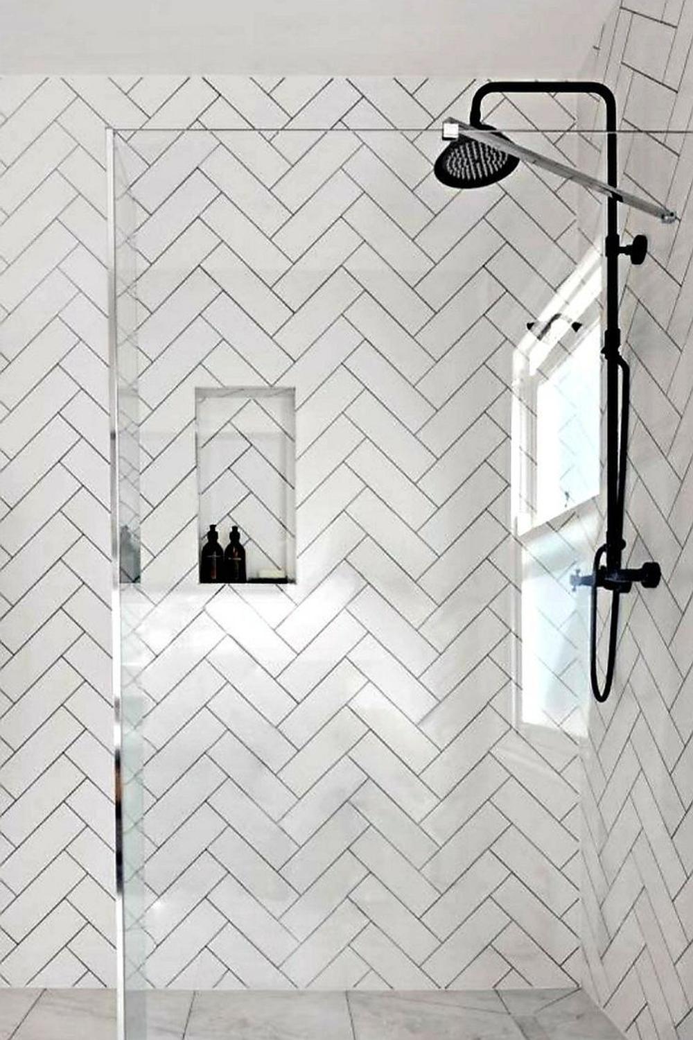 Modern bathroom shower area featuring glossy white herringbone tiles, sleek black showerhead, and glass enclosure
