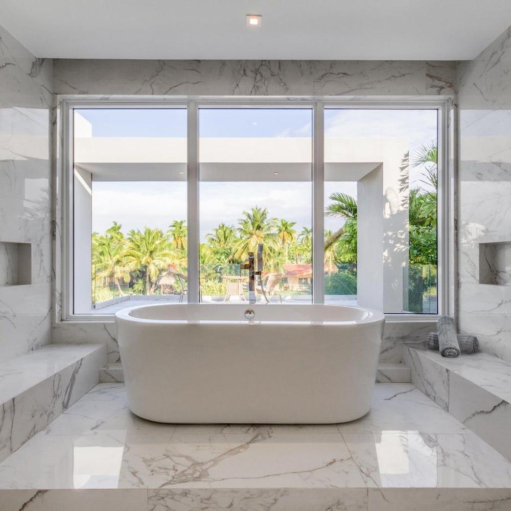 A serene bathroom featuring a freestanding tub and large windows offering an expansive view of palm trees.