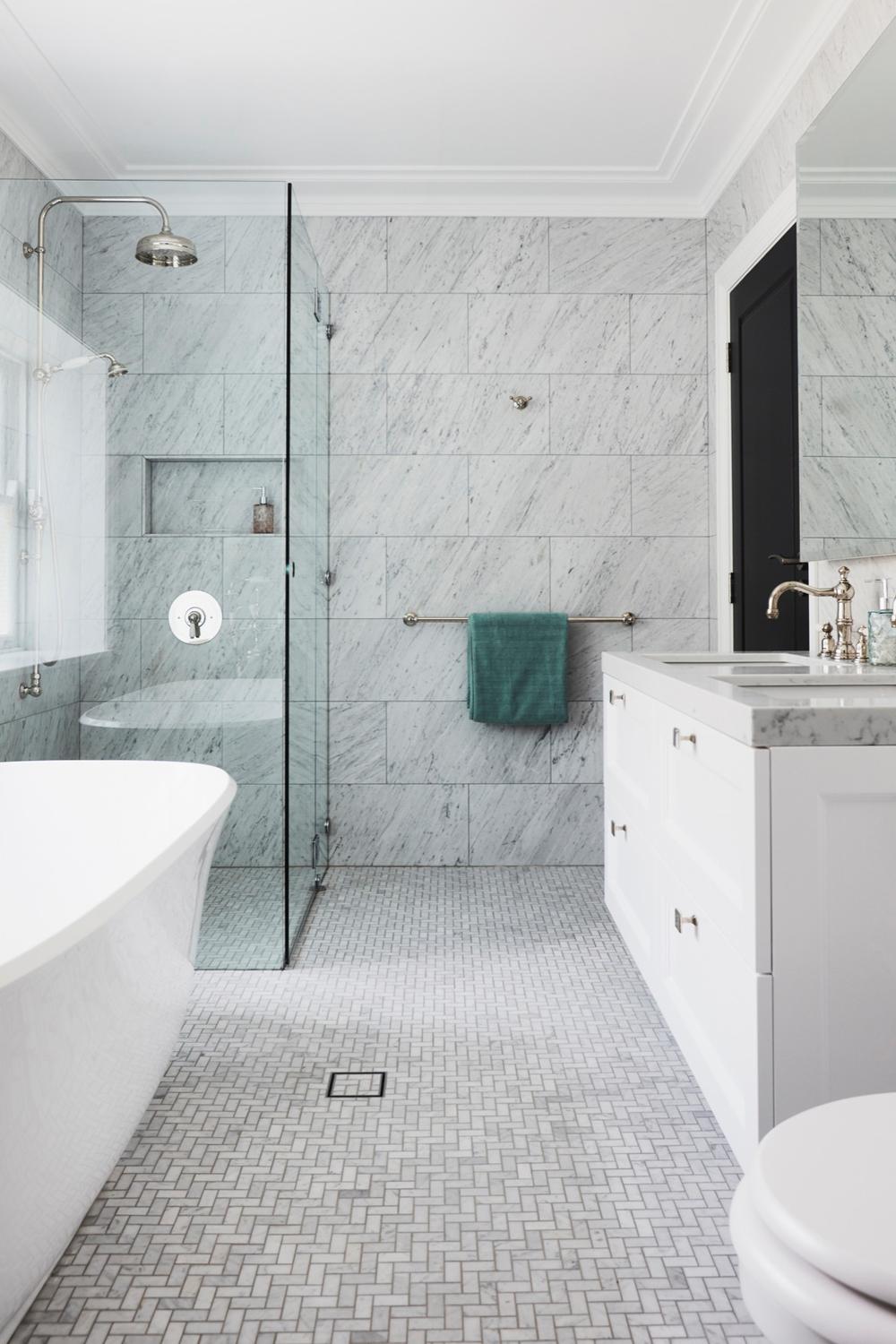 Modern bathroom featuring spacious glass shower enclosure and elegant white marble tiles with chic accessories.