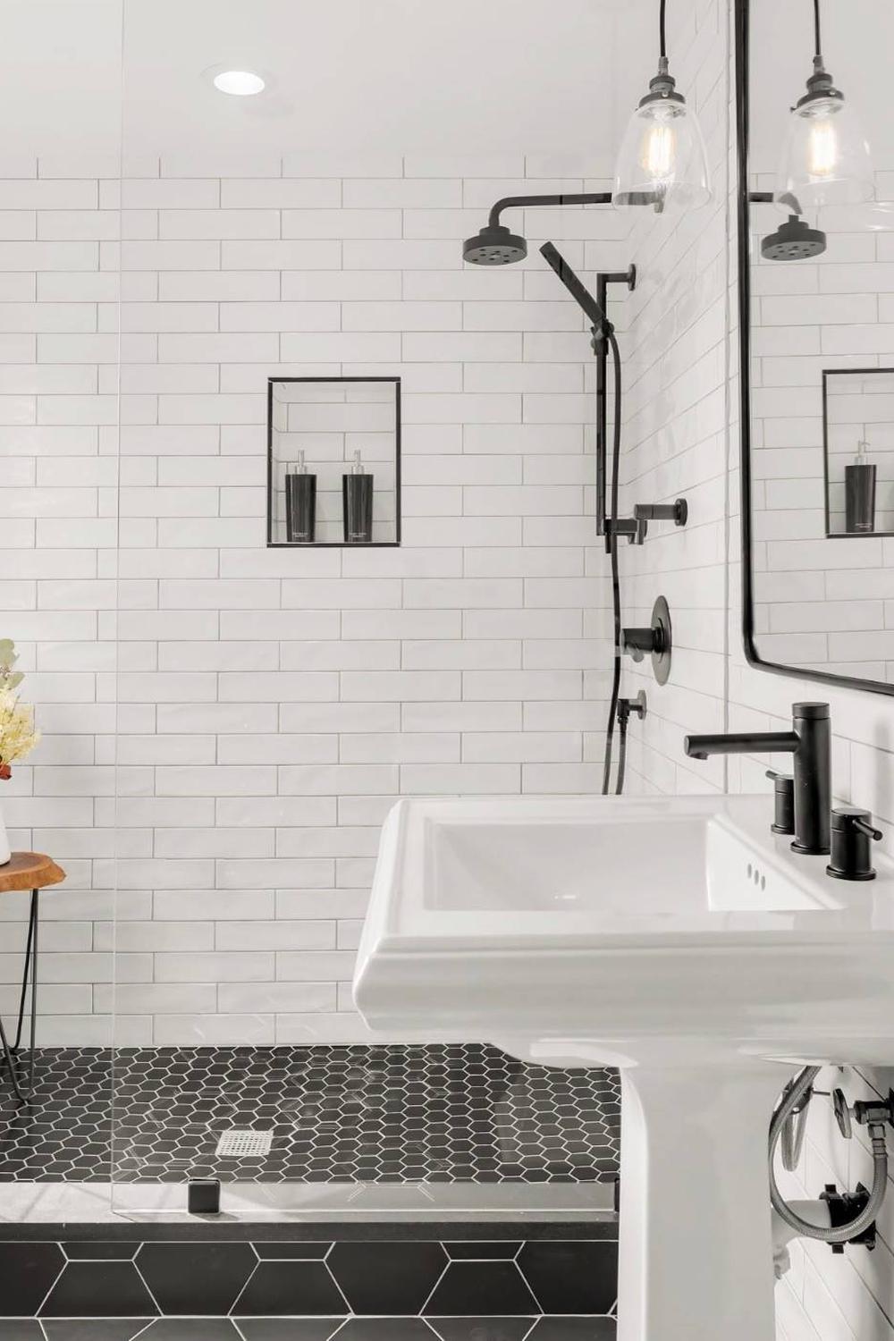 Chic modern bathroom design showcasing glossy white subway tiles, a glass shower, black fixtures, and dark hexagonal flooring.