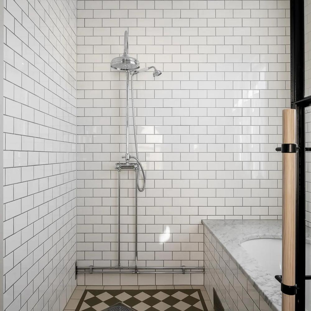 Modern minimalist bathroom design with a sophisticated tub area, glossy white subway tiles, and geometric flooring.