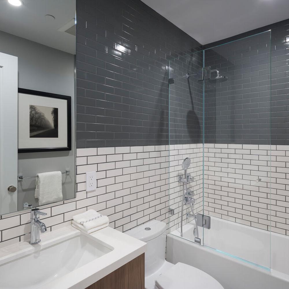 Modern bathroom featuring white tiles and black grout with black and white artwork and a wooden vanity
