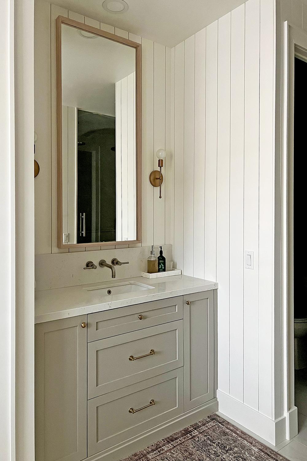 Contemporary bathroom featuring white vertical shiplap walls, soft gray vanity, and stylish lighting fixtures.