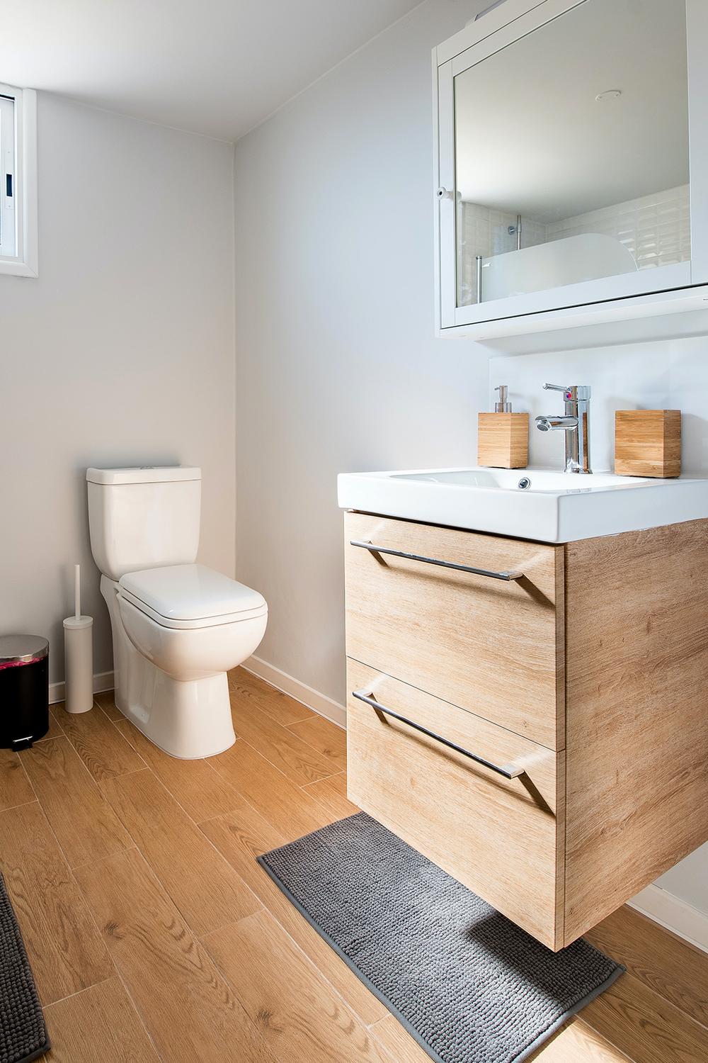 Minimalist bathroom featuring light wood flooring, a sleek vanity, and a spacious mirror.