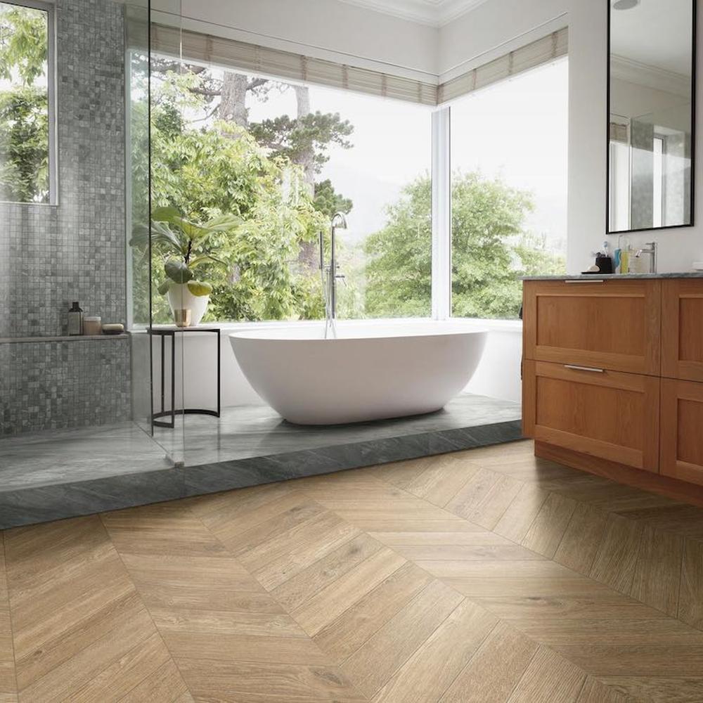 Elegant modern bathroom with a chevron wood tile floor, freestanding white bathtub, and large windows for natural light.